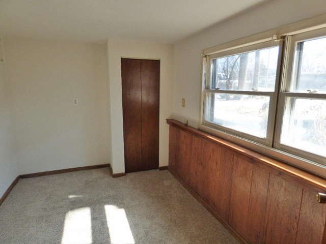 unfurnished bedroom featuring a closet, multiple windows, light colored carpet, and baseboards