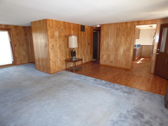 unfurnished living room with wooden walls, carpet flooring, and visible vents