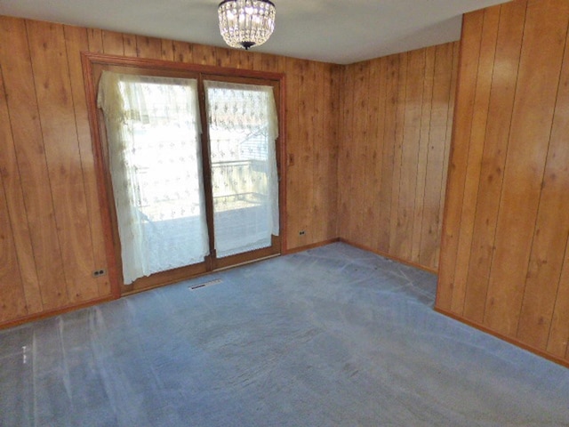 carpeted spare room featuring visible vents, a notable chandelier, and wood walls