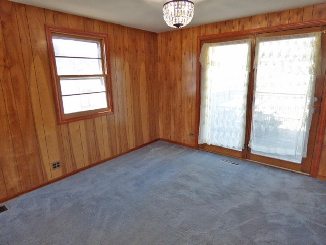 carpeted spare room with visible vents, baseboards, and wooden walls