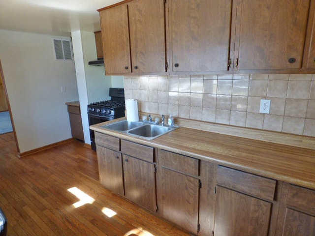 kitchen with dark wood-style floors, visible vents, black gas stove, a sink, and tasteful backsplash