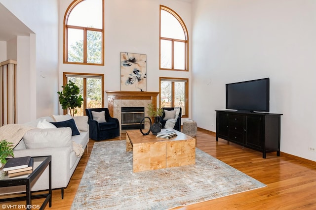 living area with a towering ceiling, a healthy amount of sunlight, light wood-style flooring, and a tiled fireplace