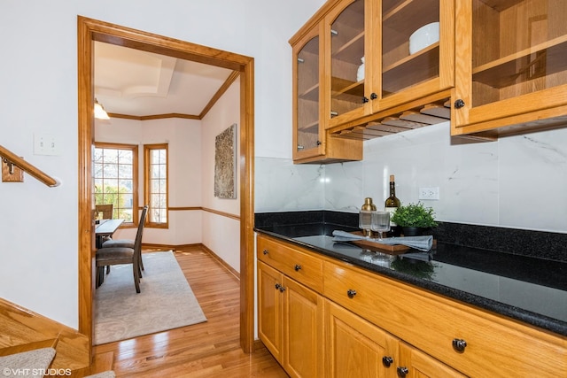 kitchen with tasteful backsplash, glass insert cabinets, baseboards, light wood-type flooring, and ornamental molding