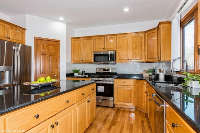 kitchen with a sink, stainless steel appliances, dark stone counters, light wood finished floors, and decorative backsplash