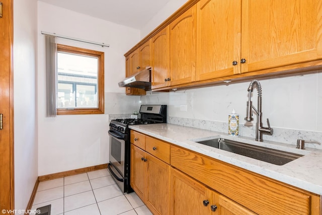 kitchen with light stone countertops, under cabinet range hood, light tile patterned flooring, stainless steel gas stove, and a sink