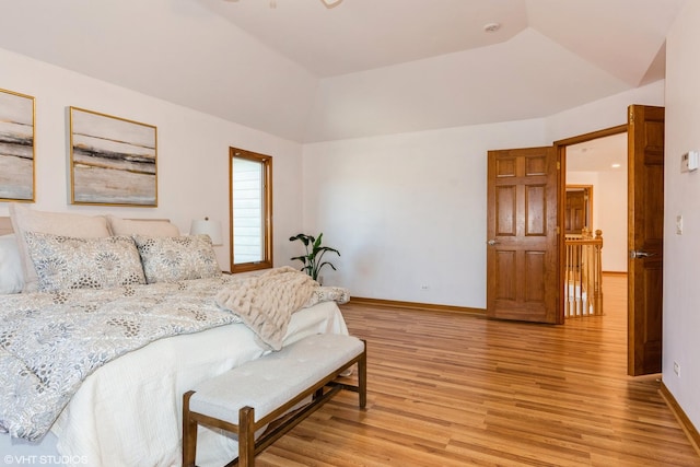 bedroom featuring baseboards, a tray ceiling, light wood-style floors, and vaulted ceiling