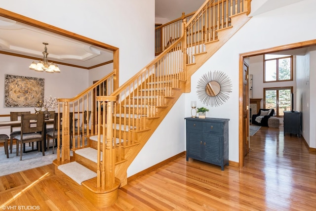 stairway with a notable chandelier, a tray ceiling, wood finished floors, baseboards, and a towering ceiling