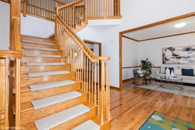 staircase featuring a high ceiling, wood finished floors, baseboards, and ornamental molding