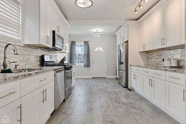 kitchen featuring marble finish floor, a sink, white cabinetry, stainless steel appliances, and light stone countertops