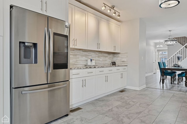 kitchen featuring a notable chandelier, light stone counters, tasteful backsplash, stainless steel fridge, and white cabinets