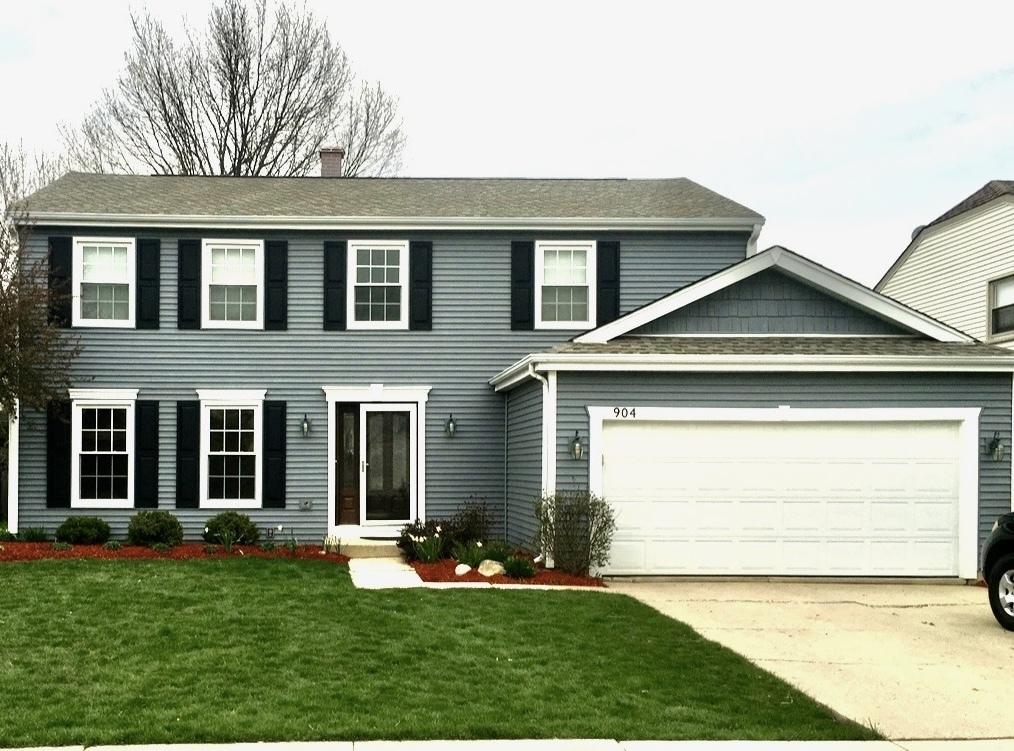 colonial house with a front yard, roof with shingles, driveway, a chimney, and a garage