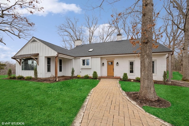 view of front of house with board and batten siding, a front lawn, a shingled roof, and a chimney