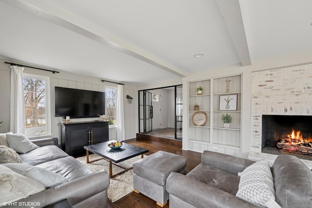 living room featuring wood finished floors, a fireplace, and beam ceiling