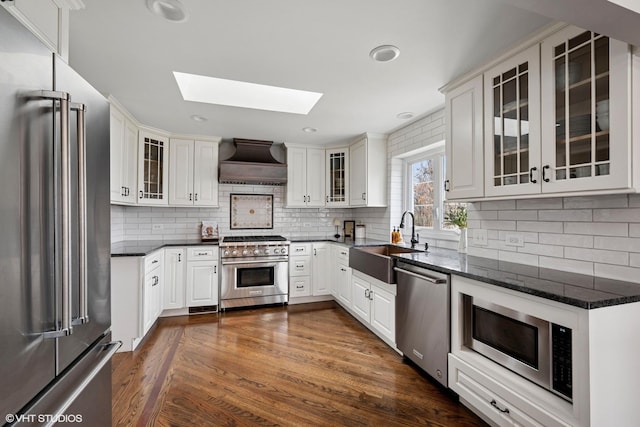 kitchen with a skylight, a sink, high quality appliances, custom range hood, and dark wood-style floors