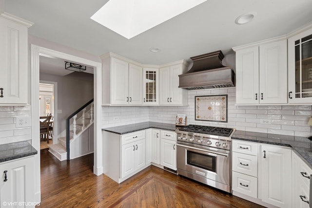 kitchen featuring custom range hood, stainless steel stove, glass insert cabinets, white cabinetry, and dark wood finished floors