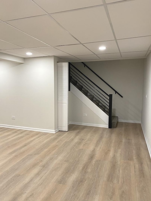 finished below grade area with stairway, baseboards, light wood-style floors, and a drop ceiling