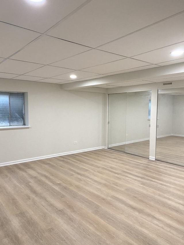 finished basement with baseboards, light wood-type flooring, and a paneled ceiling