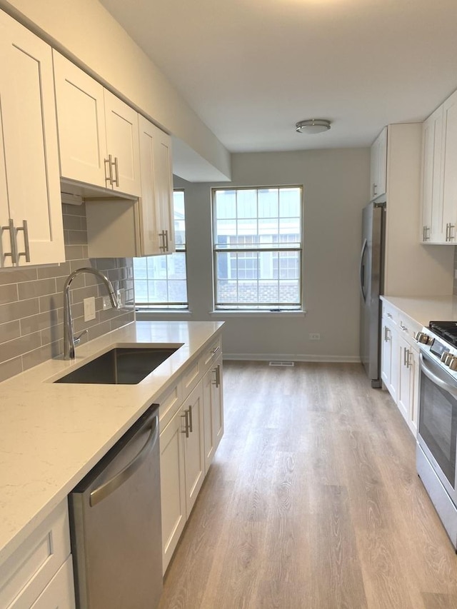 kitchen featuring light stone counters, decorative backsplash, stainless steel appliances, white cabinetry, and a sink