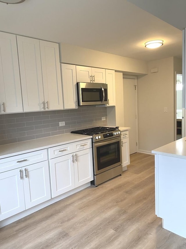 kitchen with light wood-type flooring, light countertops, appliances with stainless steel finishes, white cabinetry, and tasteful backsplash