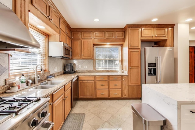 kitchen with range hood, light stone countertops, a sink, decorative backsplash, and appliances with stainless steel finishes