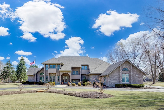 view of front of property featuring a front lawn, a balcony, brick siding, and roof with shingles