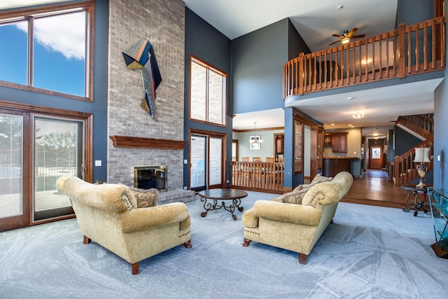 living room featuring ceiling fan, carpet, stairs, a fireplace, and a towering ceiling