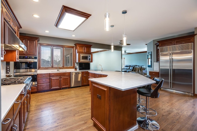 kitchen with decorative light fixtures, built in appliances, a breakfast bar area, light countertops, and a sink