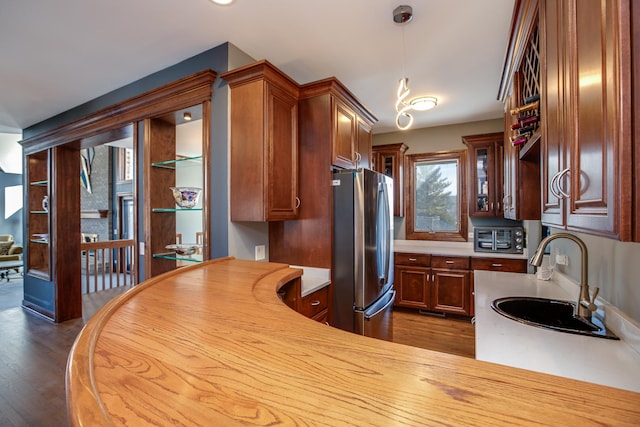 kitchen featuring a sink, glass insert cabinets, light countertops, freestanding refrigerator, and dark wood-style flooring