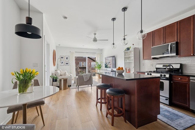 kitchen featuring a ceiling fan, stainless steel appliances, decorative backsplash, dark countertops, and a center island