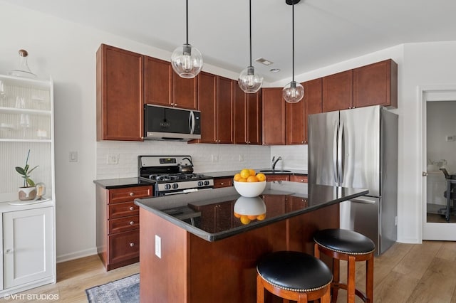 kitchen featuring light wood finished floors, backsplash, a kitchen island, appliances with stainless steel finishes, and a sink