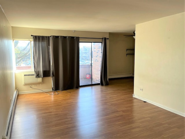 unfurnished room with baseboards, baseboard heating, an AC wall unit, and wood finished floors