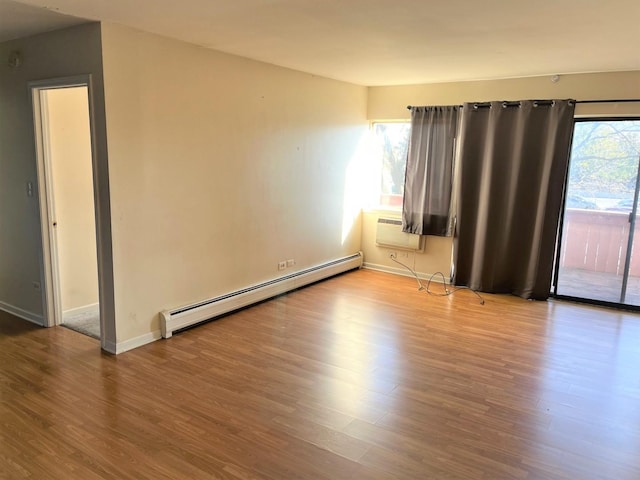 empty room featuring baseboard heating, plenty of natural light, a wall mounted AC, and wood finished floors