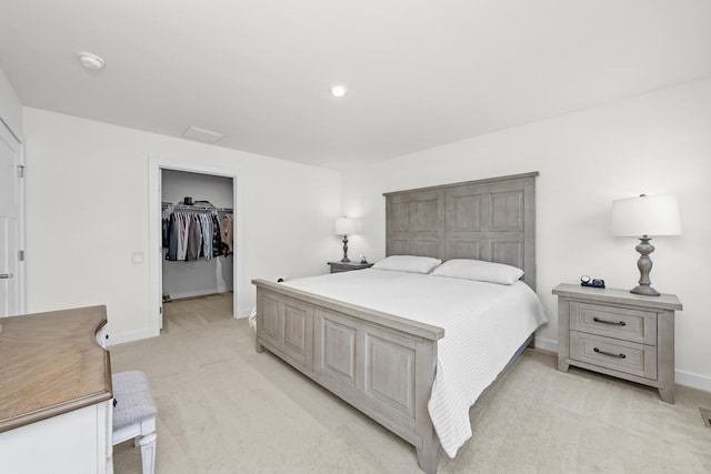 bedroom with a walk in closet, light colored carpet, and baseboards