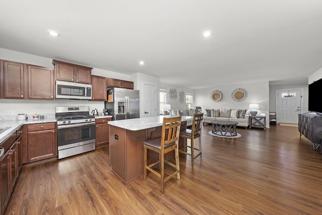 kitchen featuring open floor plan, a kitchen bar, light countertops, stainless steel appliances, and dark wood-style flooring