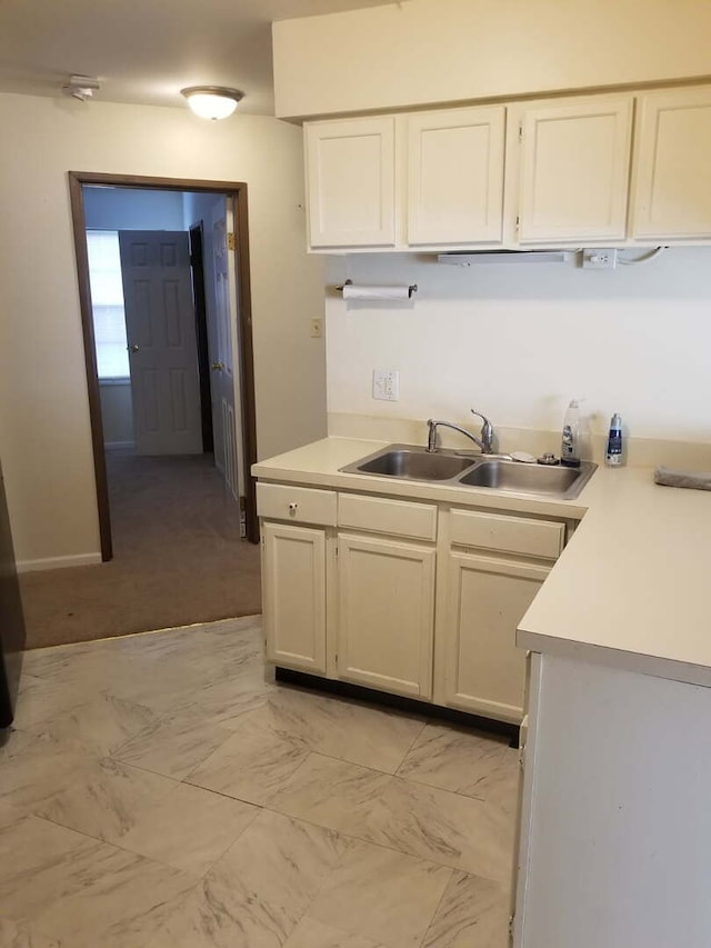 kitchen featuring light countertops, white cabinets, marble finish floor, and a sink