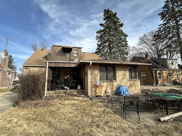 rear view of house featuring a patio, a balcony, brick siding, and roof with shingles