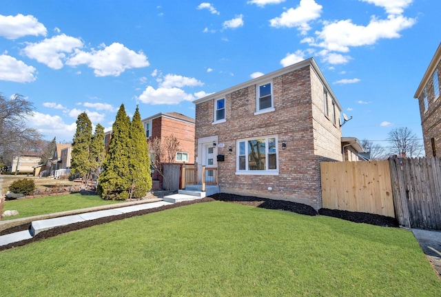 back of property with a yard, brick siding, and fence