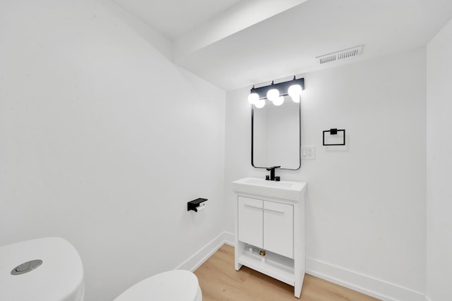 half bath with visible vents, toilet, wood finished floors, baseboards, and vanity