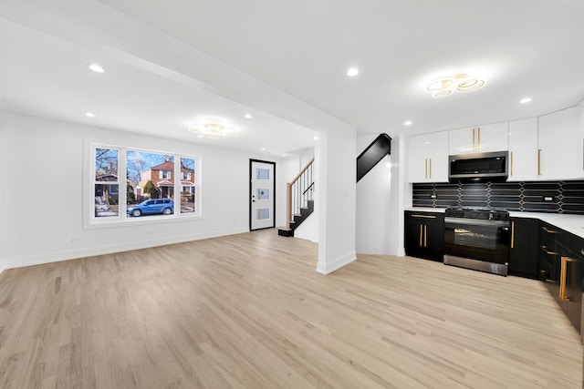 kitchen with dark cabinetry, black range with electric cooktop, light wood-style floors, stainless steel microwave, and tasteful backsplash