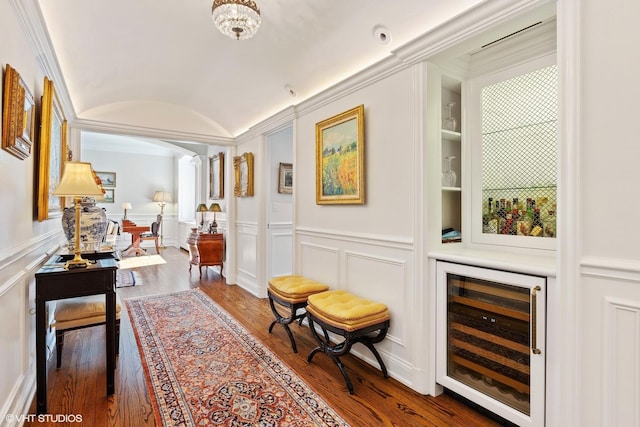 hallway with wine cooler, lofted ceiling, wood finished floors, arched walkways, and a decorative wall