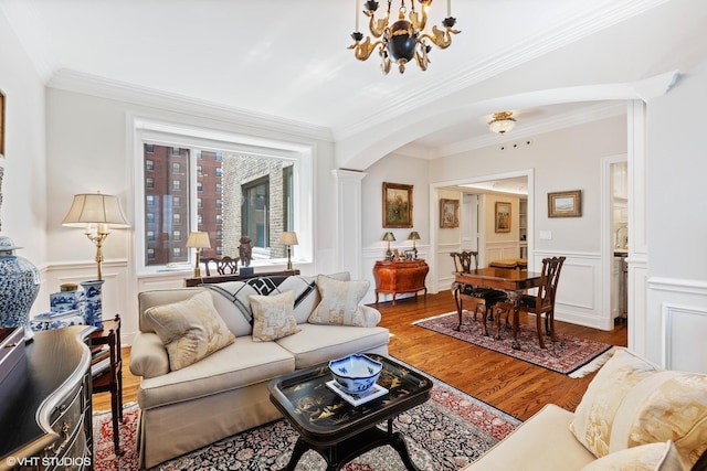 living room featuring wood finished floors, arched walkways, an inviting chandelier, wainscoting, and decorative columns