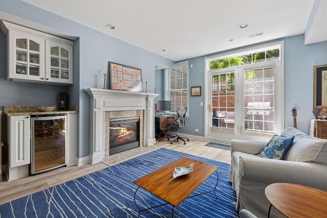 living room featuring a high end fireplace, visible vents, baseboards, wine cooler, and light wood-style flooring