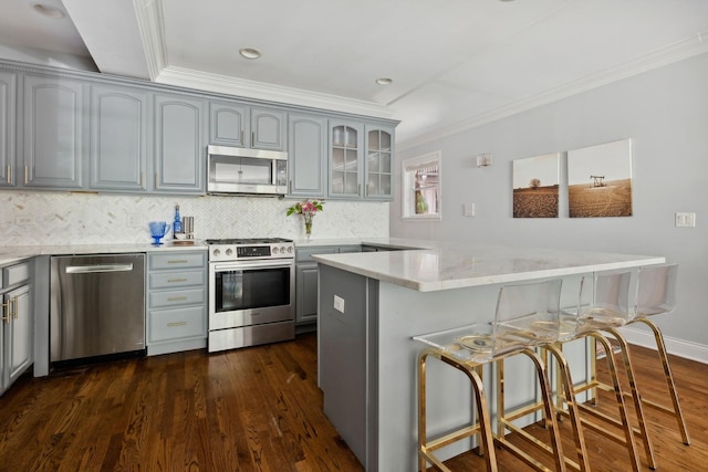 kitchen featuring stainless steel appliances, gray cabinetry, ornamental molding, and a breakfast bar