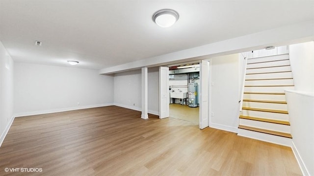 finished basement featuring baseboards, stairway, gas water heater, light wood-style flooring, and a sink