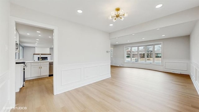 unfurnished living room with recessed lighting, light wood-type flooring, an inviting chandelier, and a wainscoted wall