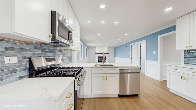 kitchen featuring a wainscoted wall, a sink, stainless steel appliances, a peninsula, and white cabinets