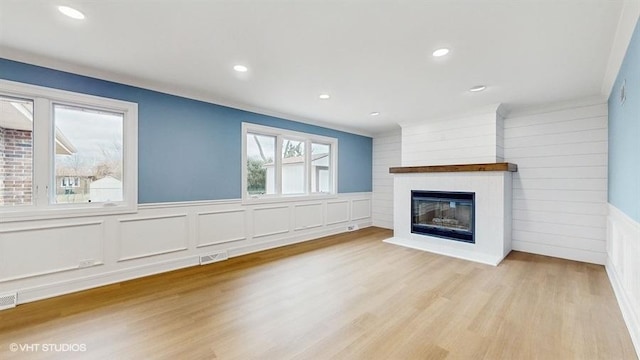 unfurnished living room featuring visible vents, a glass covered fireplace, wood finished floors, recessed lighting, and wainscoting