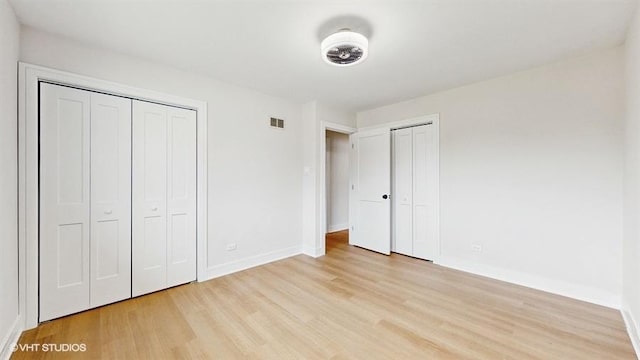 unfurnished bedroom featuring light wood finished floors, baseboards, visible vents, and two closets