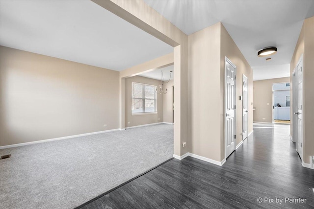 hall with visible vents, a notable chandelier, dark wood-type flooring, dark carpet, and baseboards