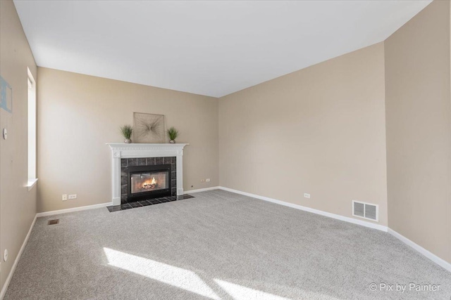 unfurnished living room with visible vents, a tile fireplace, baseboards, and carpet